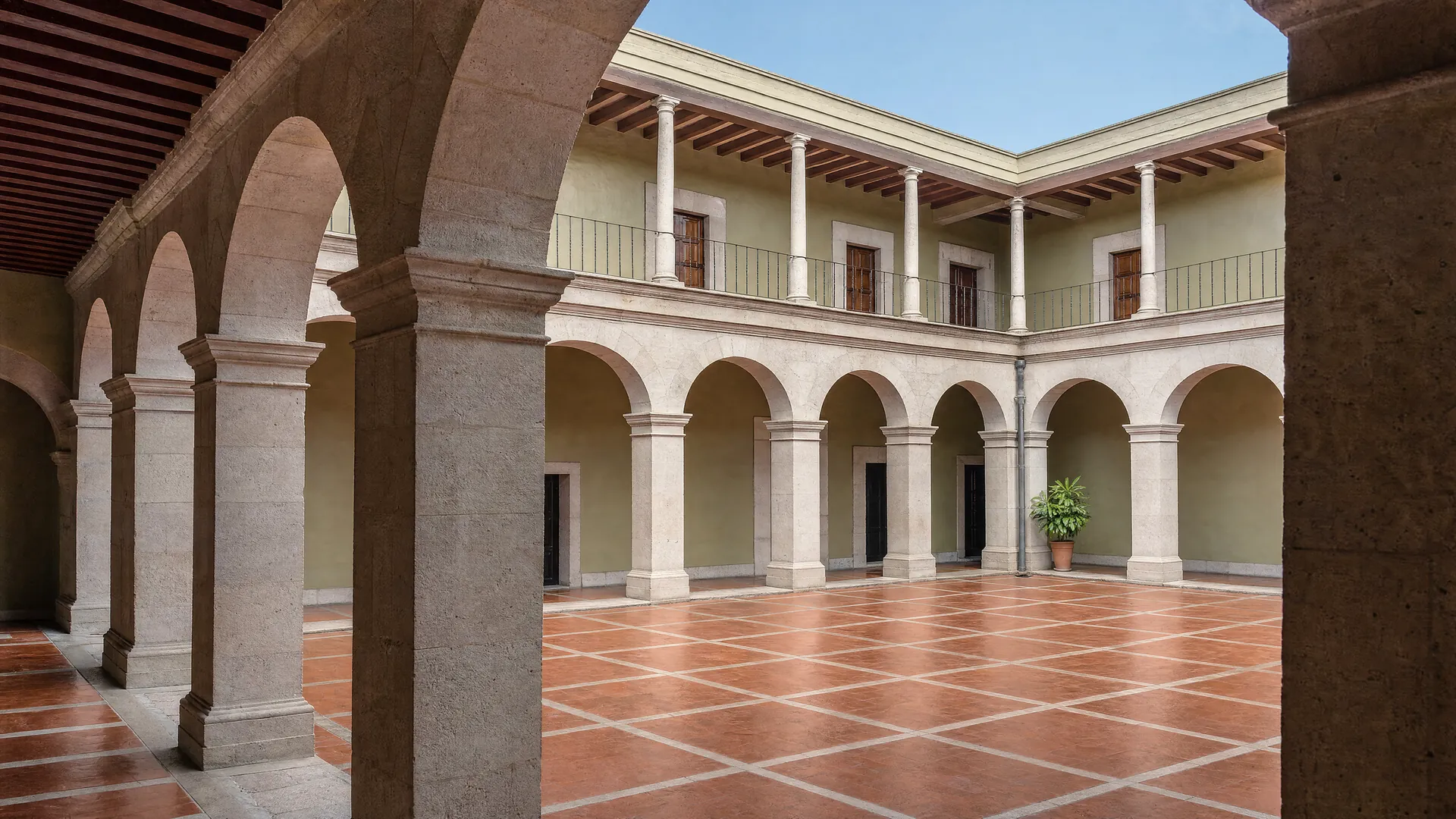 Patio interior vacío con arcos de cantera y piso de barro al mediodía
