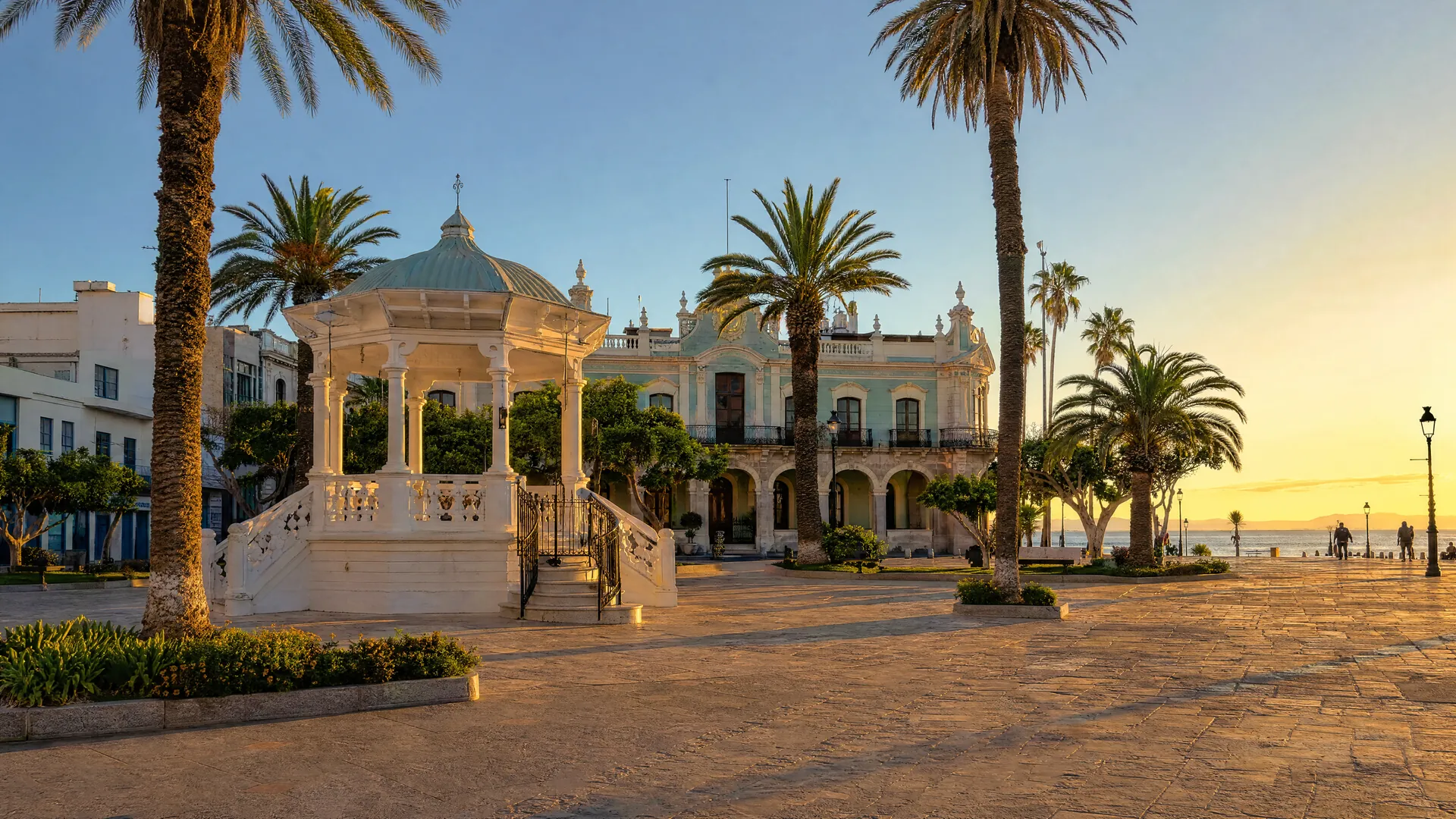 Plaza colonial en La Paz al atardecer, con kiosco blanco, palmeras y un edificio de gobierno de fachada pastel con arcos.