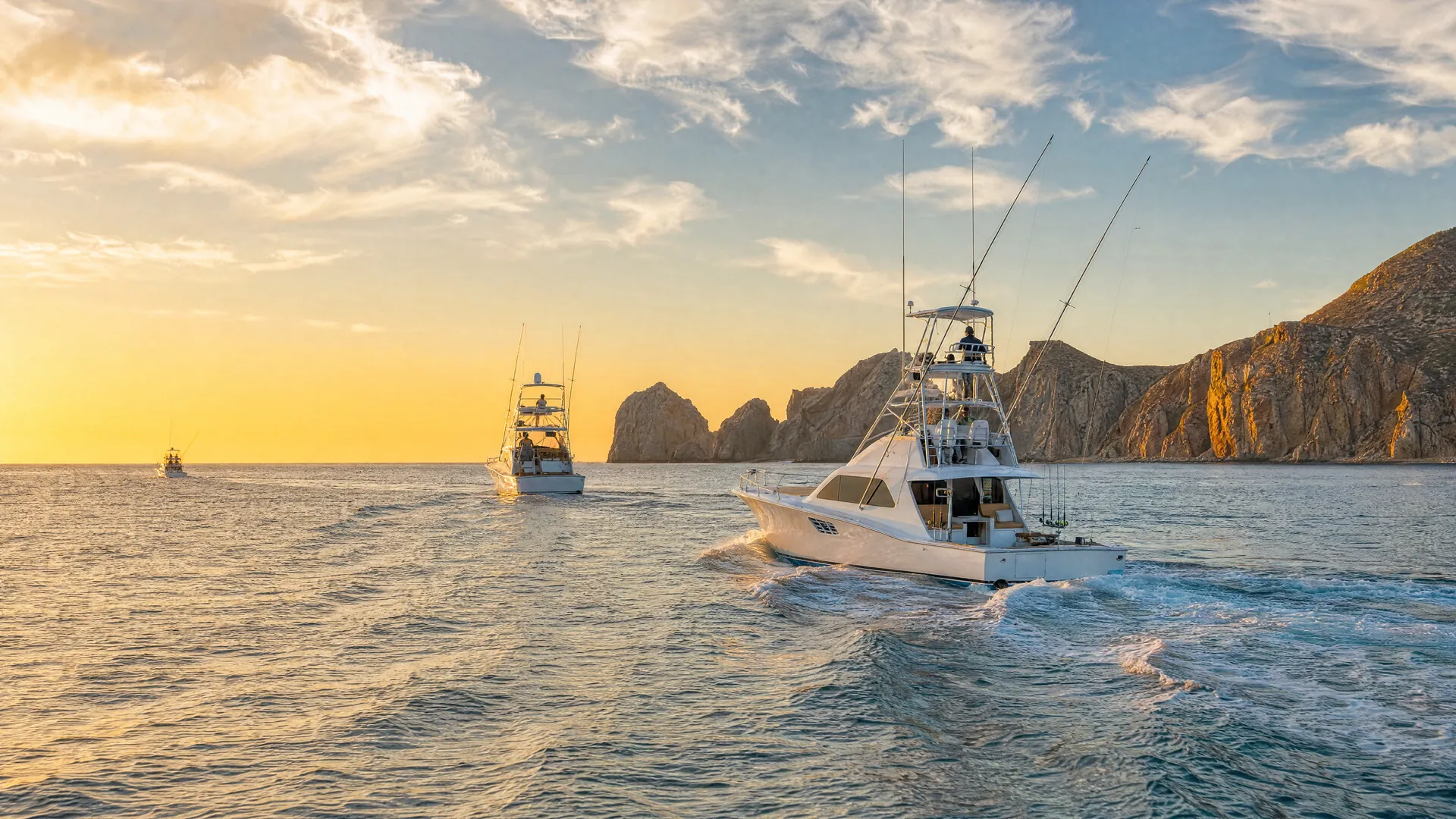Lanchas de pesca deportiva salen al amanecer de una marina en Los Cabos hacia el mar, con formaciones rocosas al fondo.