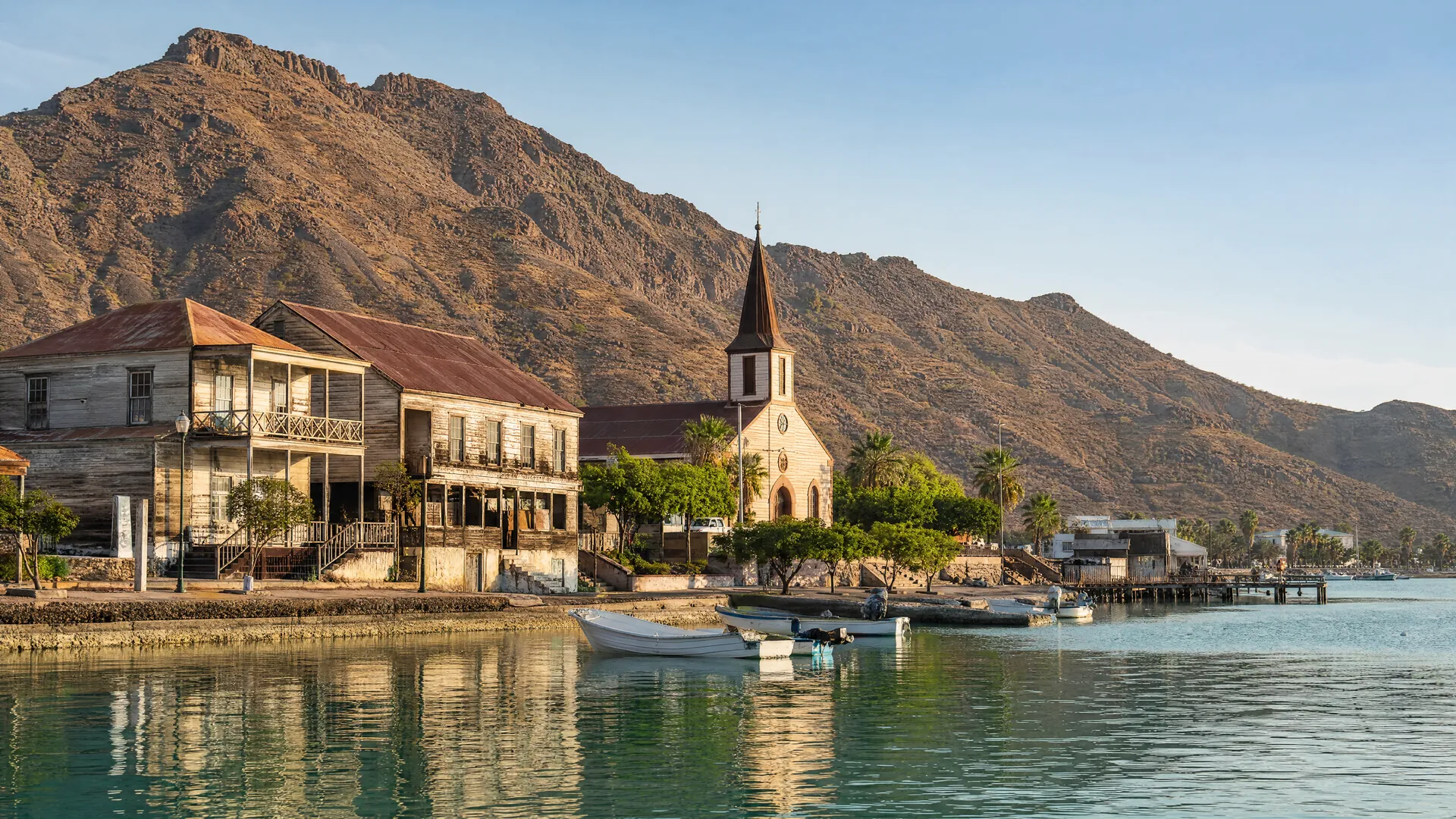 Vista matutina de Santa Rosalía con casas de madera y una iglesia junto al Golfo de California, rodeadas de cerros áridos