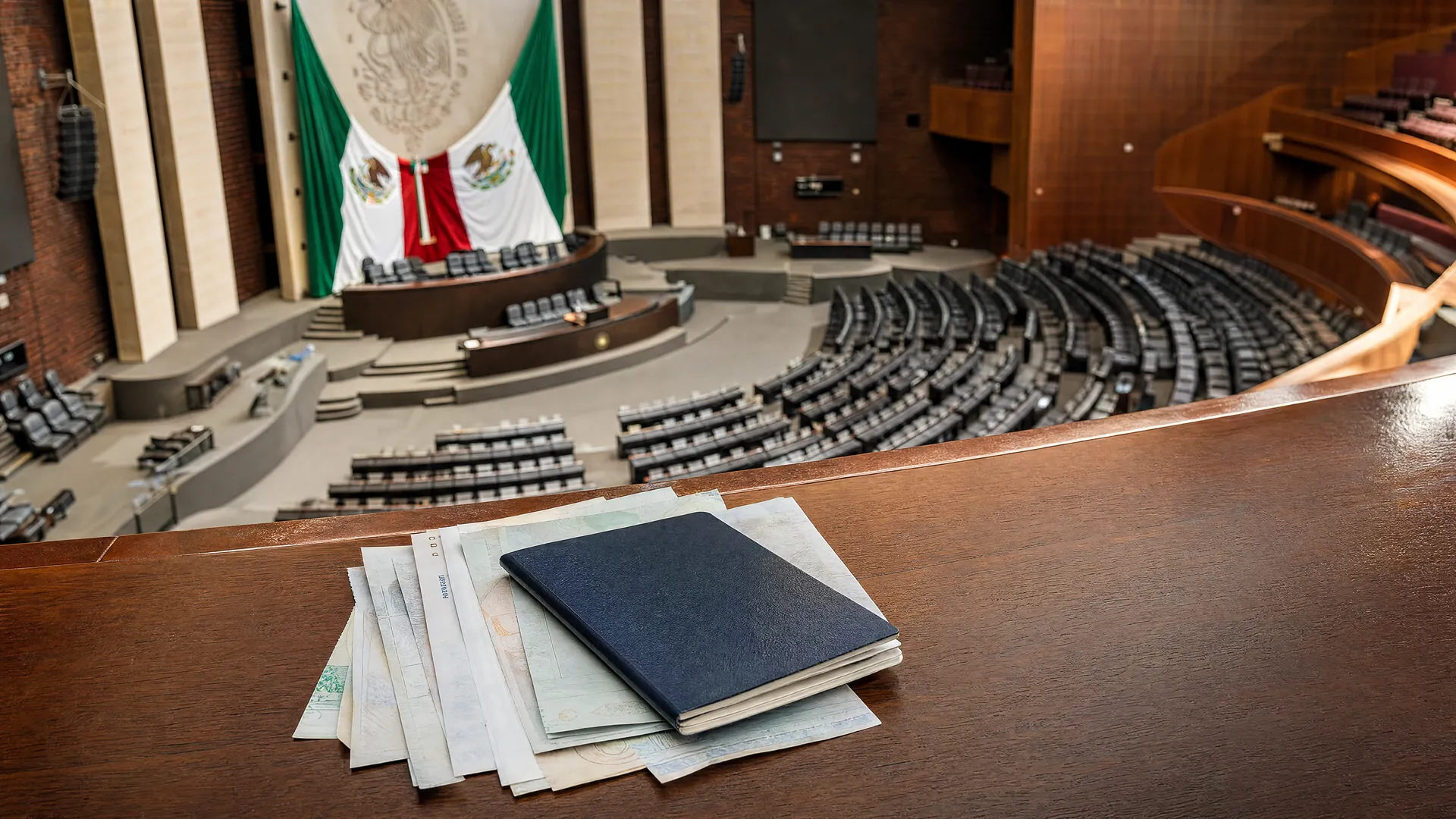 Recinto vacío de la Cámara de Diputados con un pasaporte y comprobantes de entrada de turistas sobre un escritorio en primer plano.