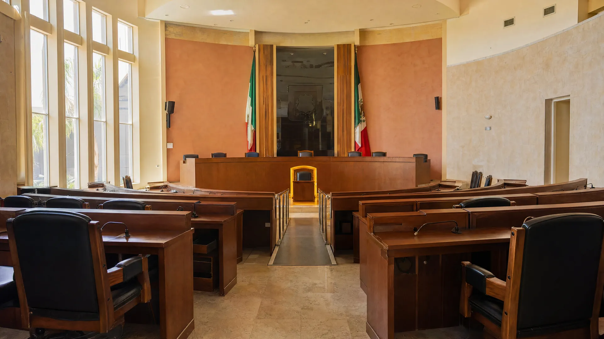 Sala legislativa vacía con curules de madera y una rampa accesible que lleva a un escaño iluminado por la luz de la mañana