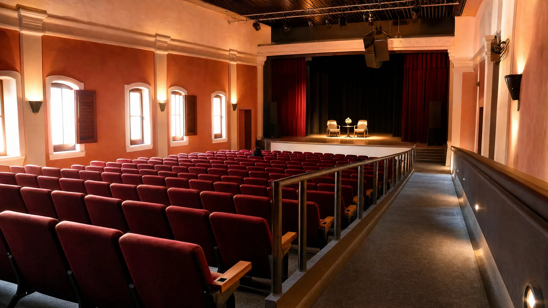 Interior de un teatro en La Paz con butacas vacías, escenario iluminado con dos sillas y una rampa de acceso para sillas de ruedas.